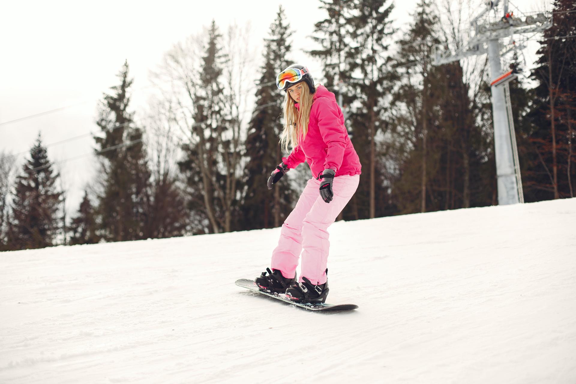 Girl snowboarding under a lift wearing a bright pink ski outfit
